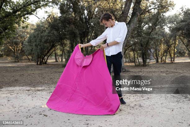 slim male bullfighter in black pants and white shirt holding pink and yellow cloak performing gracefully before corrida in nature - bullfighter stock pictures, royalty-free photos & images