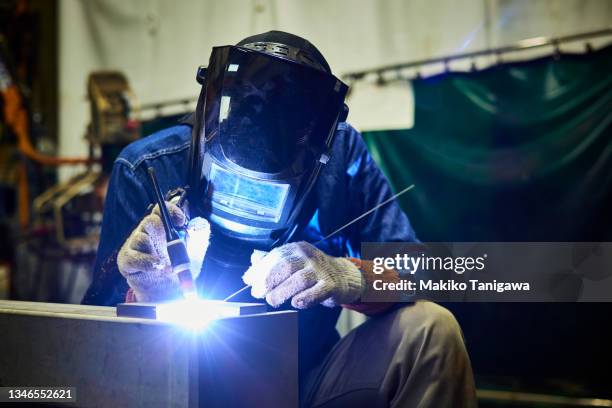 mature male welder working in a small welding factory - soldar fotografías e imágenes de stock