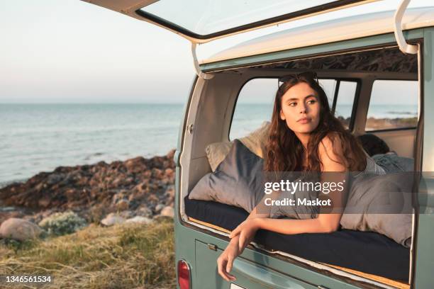 woman looking away while lying in camping van during sunset - midsummer sweden stock-fotos und bilder