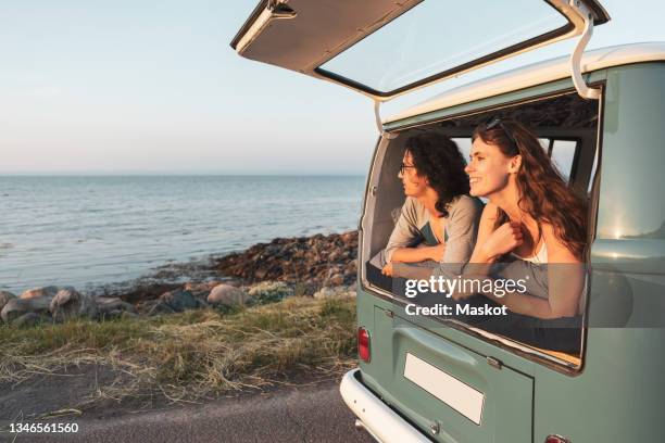 female and male friends looking at sea from camping van during road trip - midsummer sweden stock-fotos und bilder