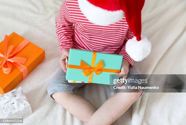 a kid in a red santa hat unpacking christmas gifts - funny gifts photos et images de collection