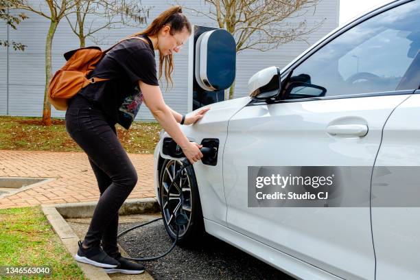 woman near the electric refueling station carrying her car - hybrid car stock pictures, royalty-free photos & images