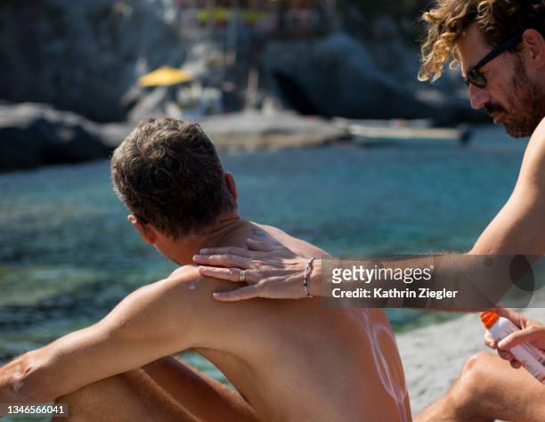man putting suntan lotion on his partner's back - putting lotion stock pictures, royalty-free photos & images