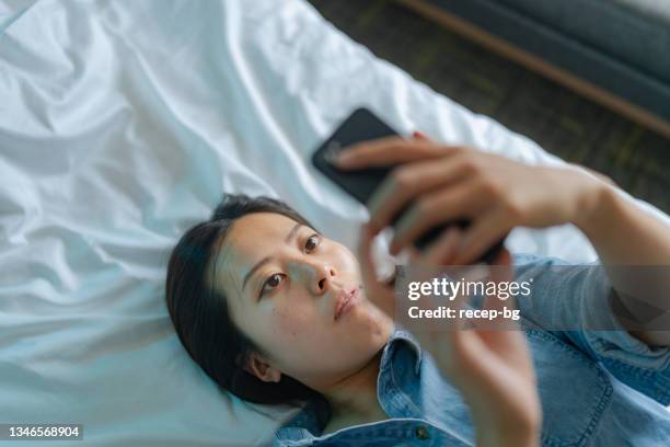 high angle view of young woman using smart phone while lying down on her bed - smart phone angle stock pictures, royalty-free photos & images