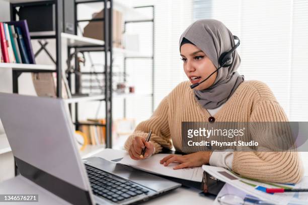 dame islamique noire en hijab et casque ayant un appel vidéo sur un ordinateur portable - femme foulard photos et images de collection