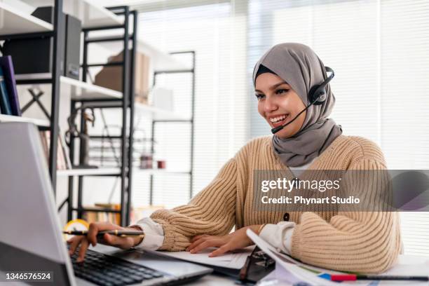 black islamic lady in hijab and headset having video call on laptop - headset imagens e fotografias de stock