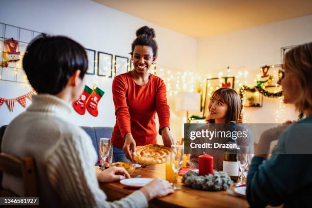 afroamerikanische millennial-frau, die weihnachtsessen für eine multiethnische gruppe von freunden serviert - man eating pie stock-fotos und bilder