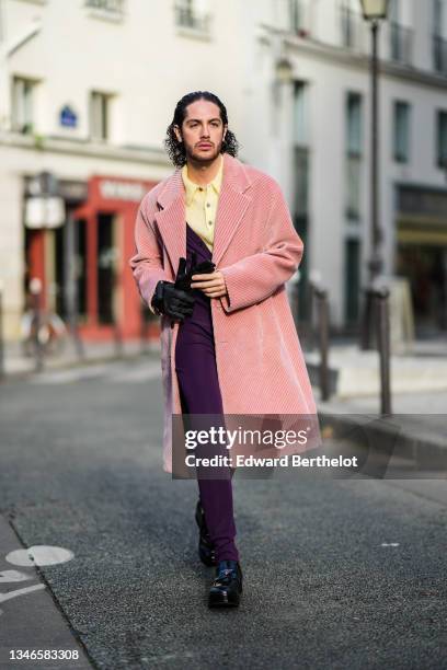 Alejandro Acero wears a pale yellow wool polo shirt, a pink ribbed velvet long coat, a purple buttoned V-neck jumpsuit, black nylon gloves, black...