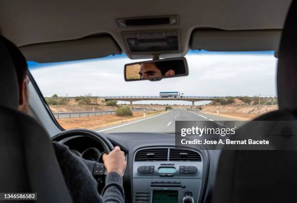 car point of view, young man driving a car on a two-lane highway. - rear view mirror stock pictures, royalty-free photos & images