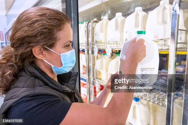 mature women shopping for milk at a supermarket wearing a protective face mask - gallon stockfoto's en -beelden