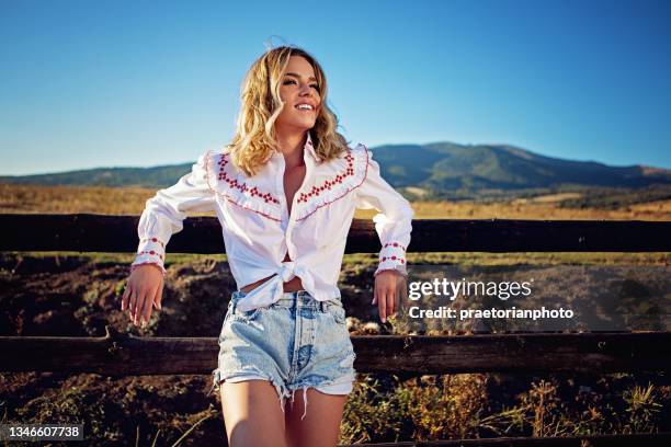 cowgirl steht auf einem zaun und genießt die aussicht - cowgirl stock-fotos und bilder