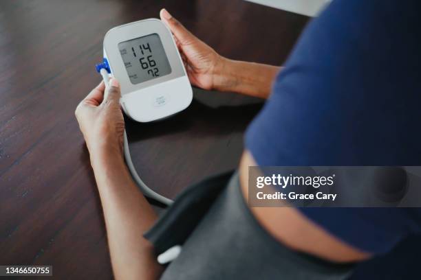 woman monitors her blood pressure - high blood pressure stock pictures, royalty-free photos & images