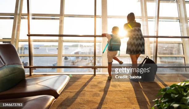 mother and son looking through window in airport terminal - family airport stock pictures, royalty-free photos & images