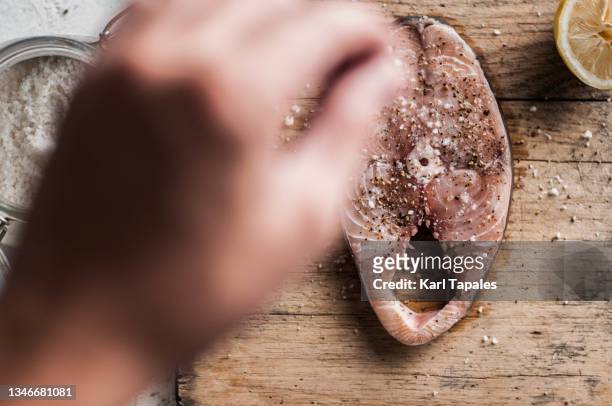 seasoning a slice of chub mackerel fish steak with lemon, salt and ground pepper on a rustic cutting board - sal de cozinha - fotografias e filmes do acervo