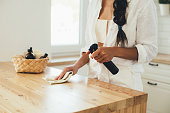 Young woman cleaning wooden table using spray and natural rag in a kitchen.