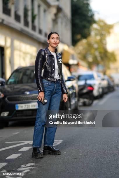 Clara Cornet wears a white t-shirt, a black leather with white logo jacket from Courreges, a white hearts leather nailed / studded shoulder bag, blue...