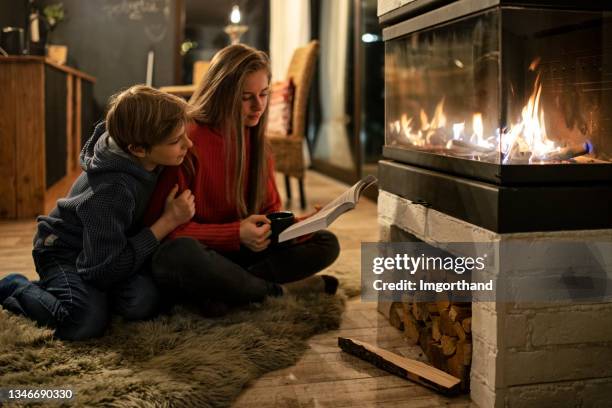 brother and sister reading by the fireplace - sitting by fireplace stock pictures, royalty-free photos & images