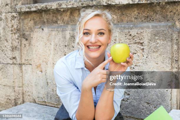 una bella adolescente con le parentesi graffe tiene una mela verde. - supporto per mensola foto e immagini stock
