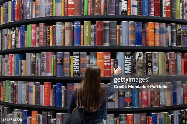 Woman from behind takes a volume from the huge bookshop at the Turin Book Fair 2021. Turin , October 14th, 2021