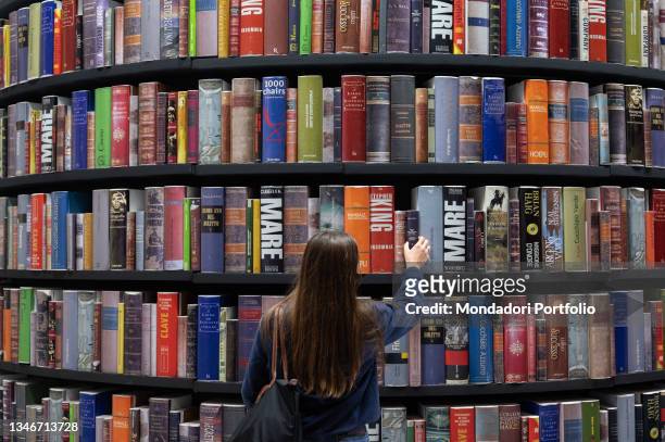 Woman from behind takes a volume from the huge bookshop at the Turin Book Fair 2021. Turin , October 14th, 2021