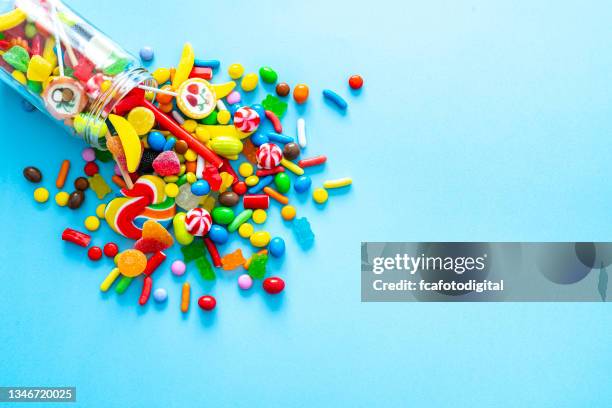 glass jar spilling candies on blue background - comida doce imagens e fotografias de stock