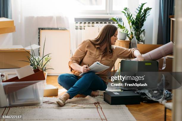 moving out: beautiful overweight woman sitting on the floor surrounded by packed boxes and making a to-do list - possession stock pictures, royalty-free photos & images