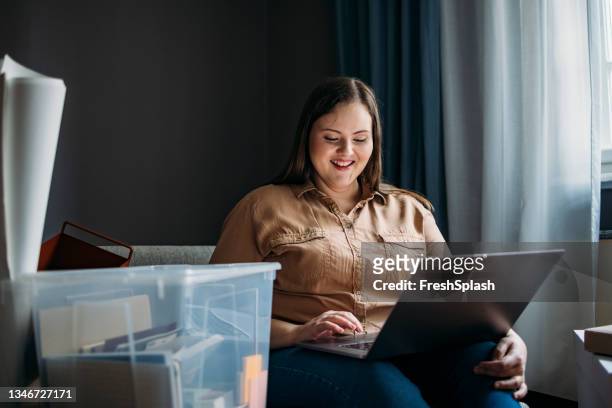 schöne lächelnde übergewichtige frau, die auf dem sofa in ihrer neuen wohnung sitzt und auf einem laptop tippt - box white flat stock-fotos und bilder