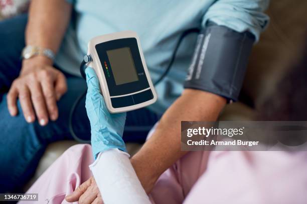 high angle shot of an unrecognizable female nurse taking a patient's blood pressure while sitting in the retirement home - high blood pressure stockfoto's en -beelden