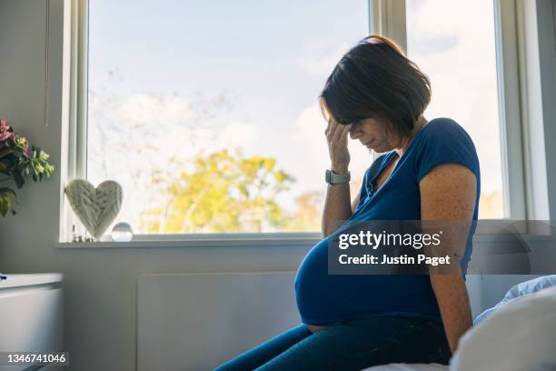 mature pregnant woman sitting on her bed - negative emotion - mujer embarazada fotografías e imágenes de stock