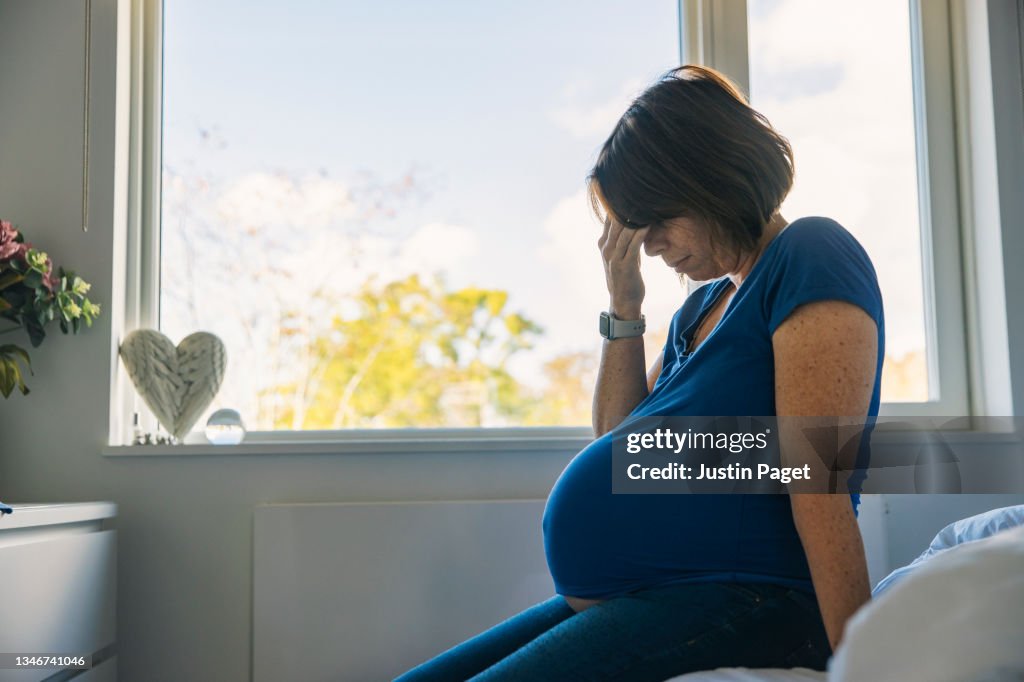Mature pregnant woman sitting on her bed - negative emotion