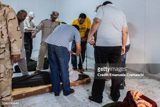 People take pictures of the corpse of Libya's ex-strongman Muammar Gaddafi, lying on the floor of the cold storage room of a former vegetable market...