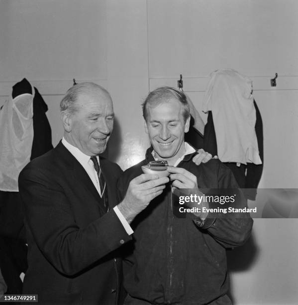 English footballer Bobby Charlton of Manchester United receives a cigarette lighter from team manager Matt Busby , UK, 5th December 1964.