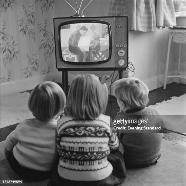 Four-year-old Claire Potter and her two-year-old twin brothers John and Hugh watch a children's television programme, UK, 26th November 1964. Their...