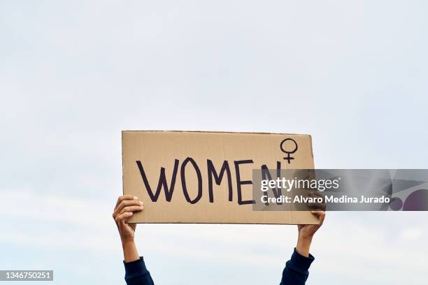 unrecognizable woman's hands holding a protest banner with the message women, with the sky in the background. - feminism stock pictures, royalty-free photos & images