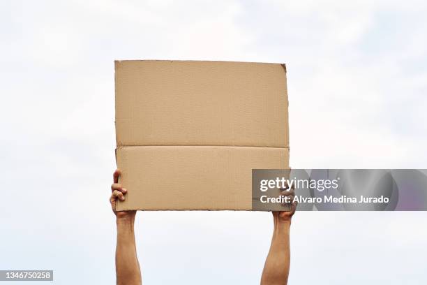 unrecognizable man hands holding a protest banner with no message, with the sky in the background. - man with cardboard sign stock pictures, royalty-free photos & images