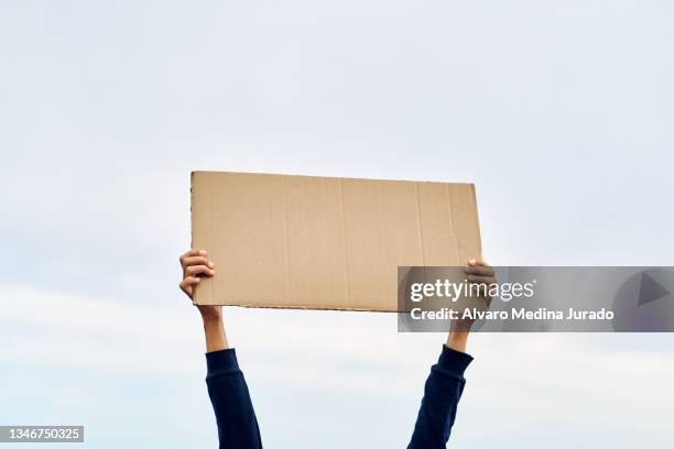 unrecognizable woman's hands holding a protest banner with no message, with the sky in the background. - manifestante fotografías e imágenes de stock