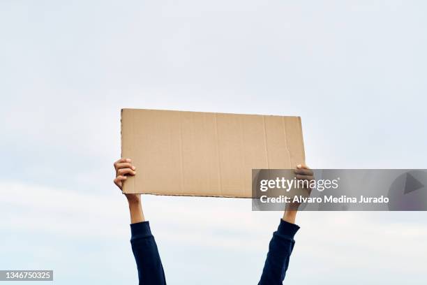 unrecognizable woman's hands holding a protest banner with no message, with the sky in the background. - plakkaat stockfoto's en -beelden