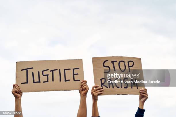 unrecognizable man and woman holding protest banners with messages to stop racism and justice, with the sky in the background. - anti racism stock pictures, royalty-free photos & images