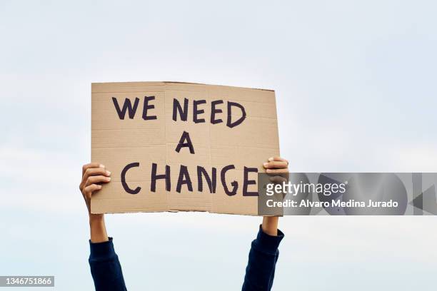 unrecognizable woman's hands holding a protest banner with the message we need a change, with the sky in the background. - placard stockfoto's en -beelden