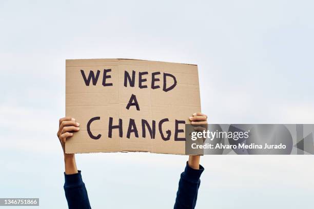 unrecognizable woman's hands holding a protest banner with the message we need a change, with the sky in the background. - sign board stock pictures, royalty-free photos & images