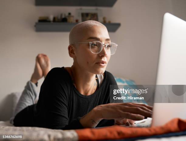 shot of a young woman using her laptop while lying on her bed - home sweet home stockfoto's en -beelden