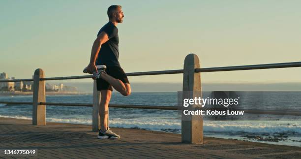 shot of a mature man stretching his legs while exercising along the promenade - beach pavilion stock pictures, royalty-free photos & images