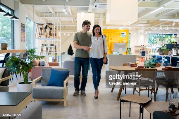 happy couple selecting items for the wedding registry at a furniture store - winkel stockfoto's en -beelden