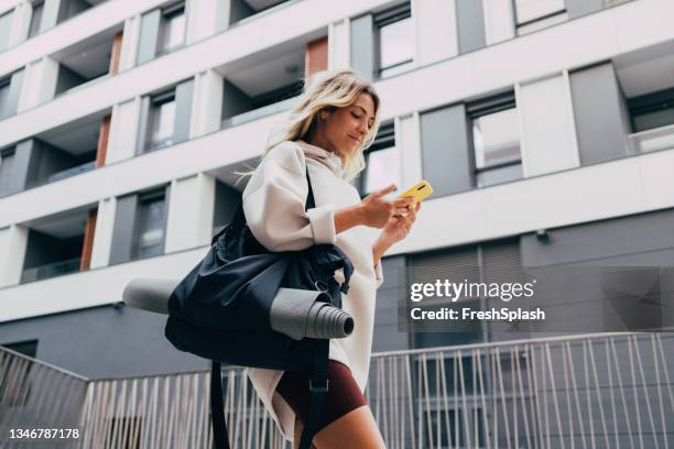 happy sporty woman in a white sweatshirt using a mobile phone outdoors - period of training stock pictures, royalty-free photos & images