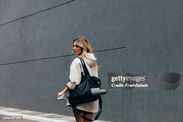 sporty woman in a white sweatshirt walking in city - duffle bag stock pictures, royalty-free photos & images