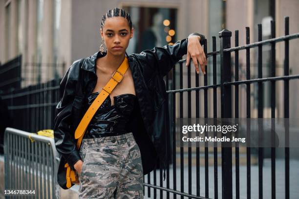 Model Daisy Oh wears a snake earrings, black jacket, black corset top, yellow cross-body bag, and green camouflage pants after the Tory Burch show on...