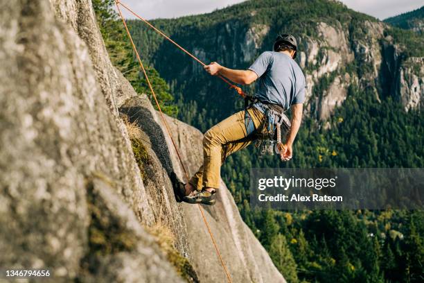 a rock climber gets lowered down a tall rock face on the end of a rope - ta ner bildbanksfoton och bilder