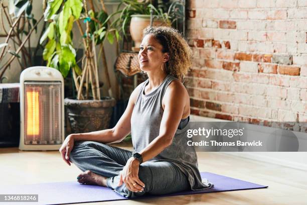 medium shot of smiling mature yoga instructor sitting in studio before class - women yoga stock pictures, royalty-free photos & images