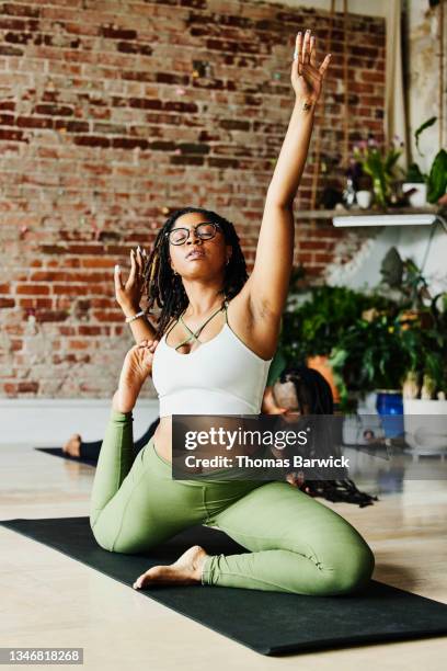 wide shot of woman moving through mermaid pose while taking class in yoga studio - african american woman barefoot stock pictures, royalty-free photos & images