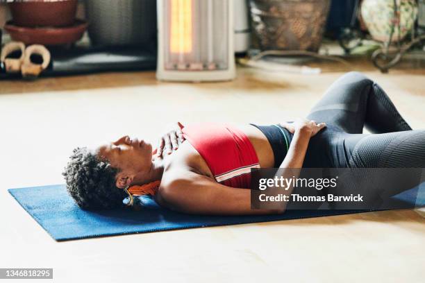 medium shot of mature woman relaxing in reclining bound angle pose during class in yoga studio - hands on chest stock pictures, royalty-free photos & images